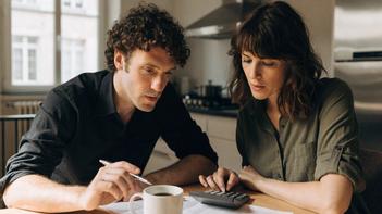 Un couple fait ses comptes à la table de la cuisine avec une calculatrice et des papiers, pour savoir si, quand mon mari touche 1500 euros, ai-je droit au RSA